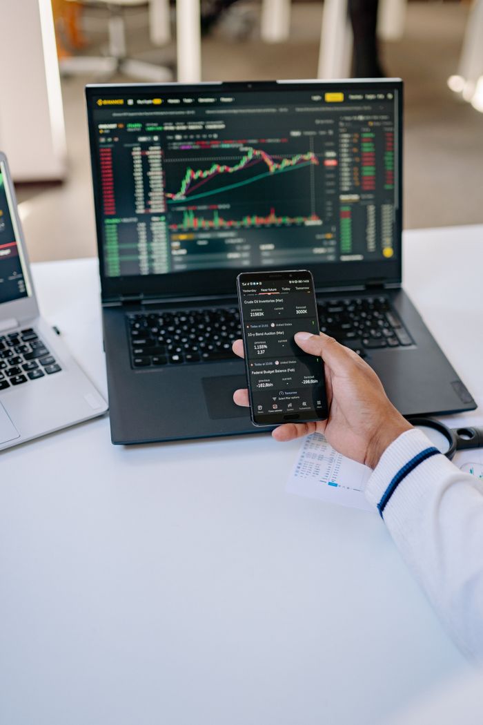 services-02 Person analyzing stock market data on a laptop and smartphone at a desk.